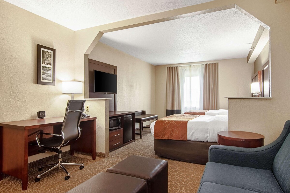 A hotel room with a desk, chair, bed, and a TV.