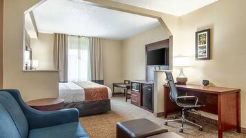 Habitación de hotel con cama, escritorio, silla, televisor y lámpara.