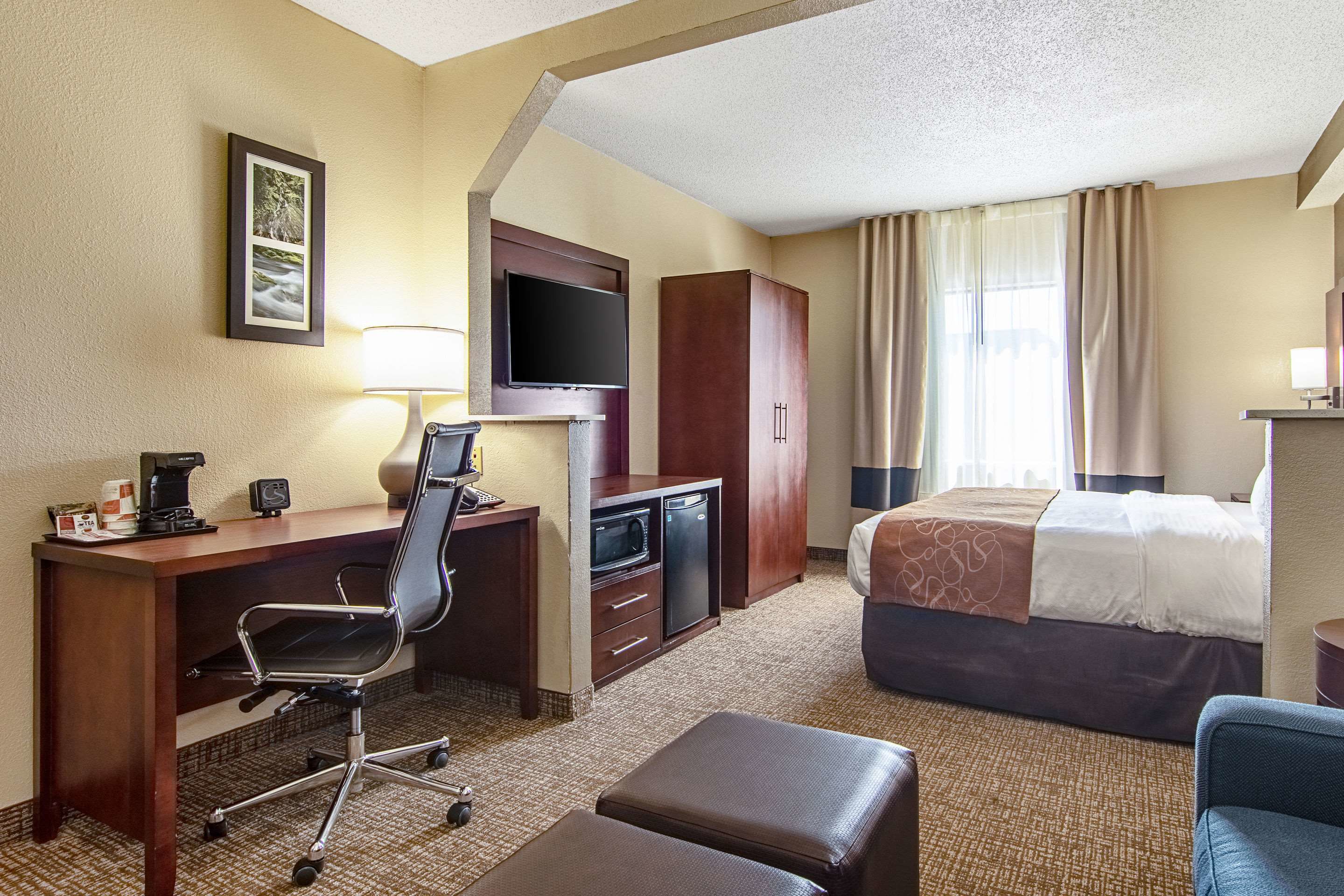 A hotel room with a bed, desk, chair, television, and a small kitchenette.