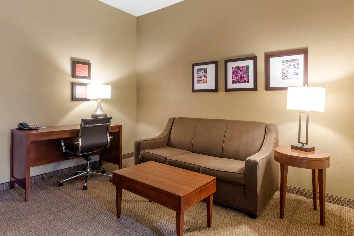 A hotel room with a wooden desk, a leather sofa, a wooden coffee table, and two wall-mounted lamps.
