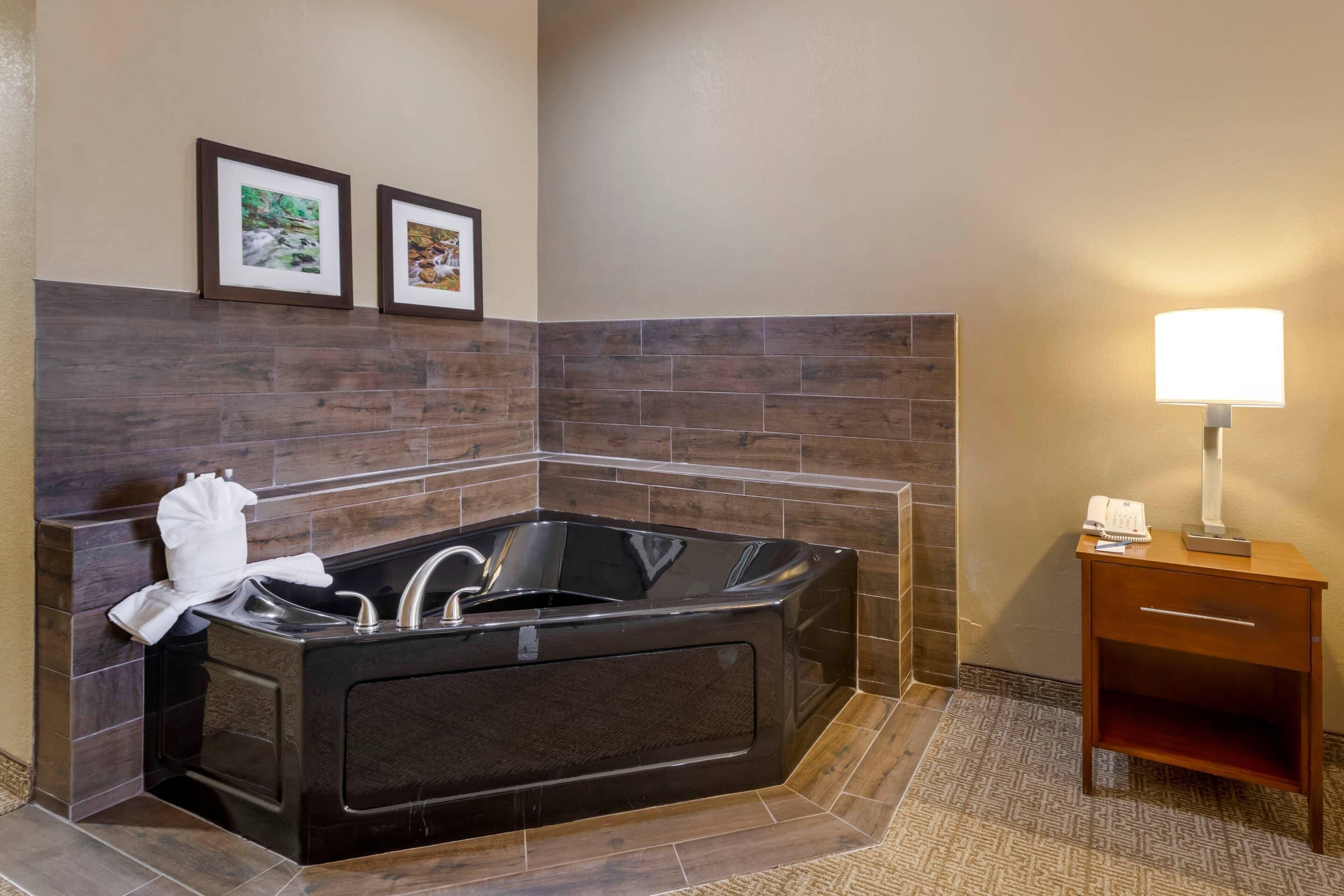 Une salle de bain moderne avec une grande baignoire noire, une table d’appoint en bois avec une lampe, et deux tableaux encadrés accrochés au mur.