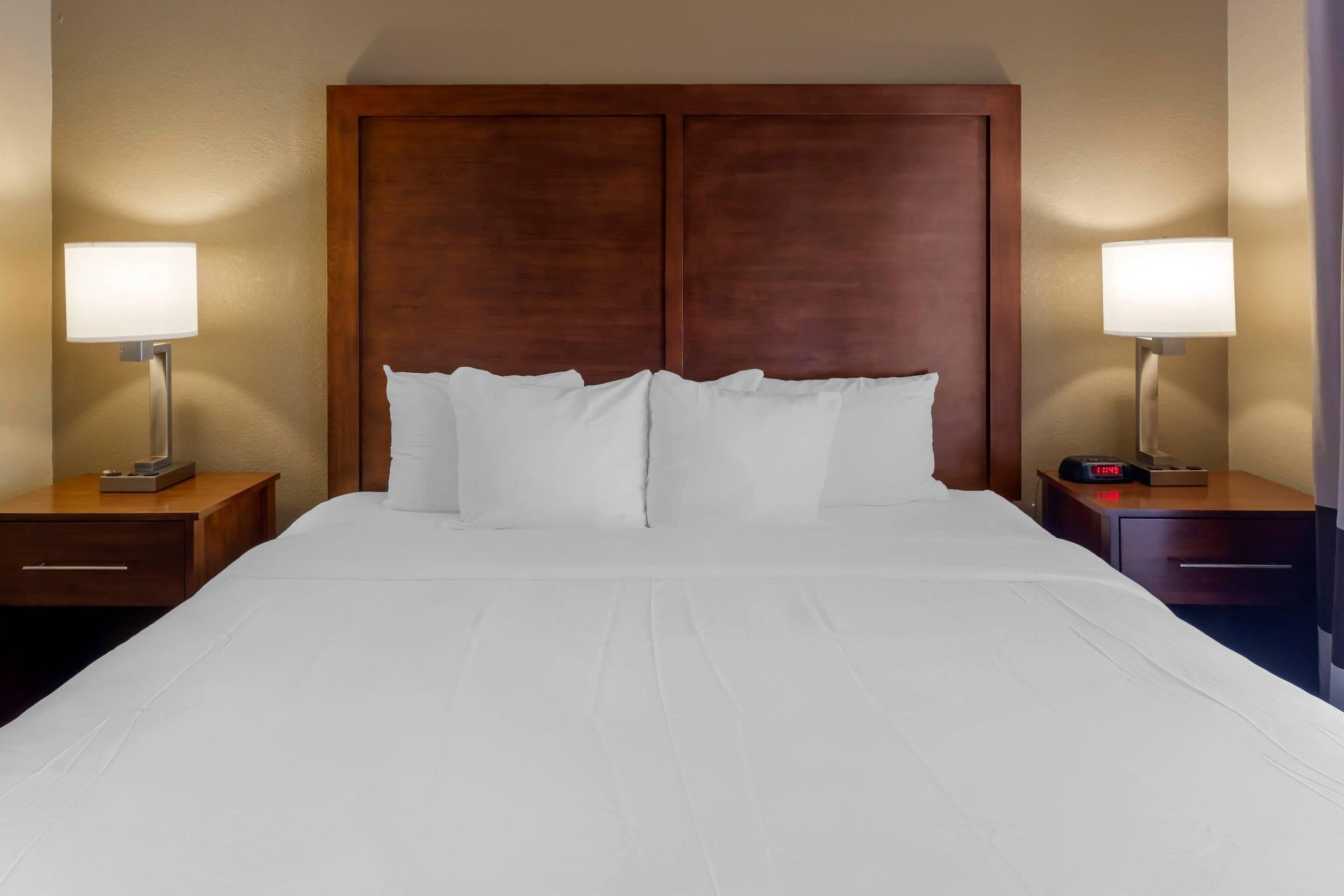 Une chambre d’hôtel avec un grand lit, deux tables de chevet et deux lampes fixées au mur.
