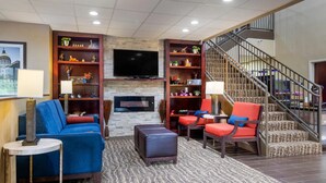 A modern living room with a fireplace, a large flat-screen TV, a blue sofa, a red armchair, and a staircase. - Comfort Inn & Suites Peachtree Corners - Norcross (Norcross)
