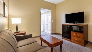 A hotel room with a sofa, a small table, a lamp, a television, and a microwave. - Comfort Inn & Suites Peachtree Corners - Norcross (Norcross)
