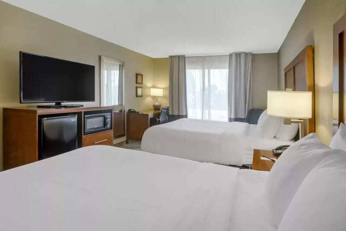 A hotel room with two beds, a television, a desk with a lamp, and a window with curtains.
