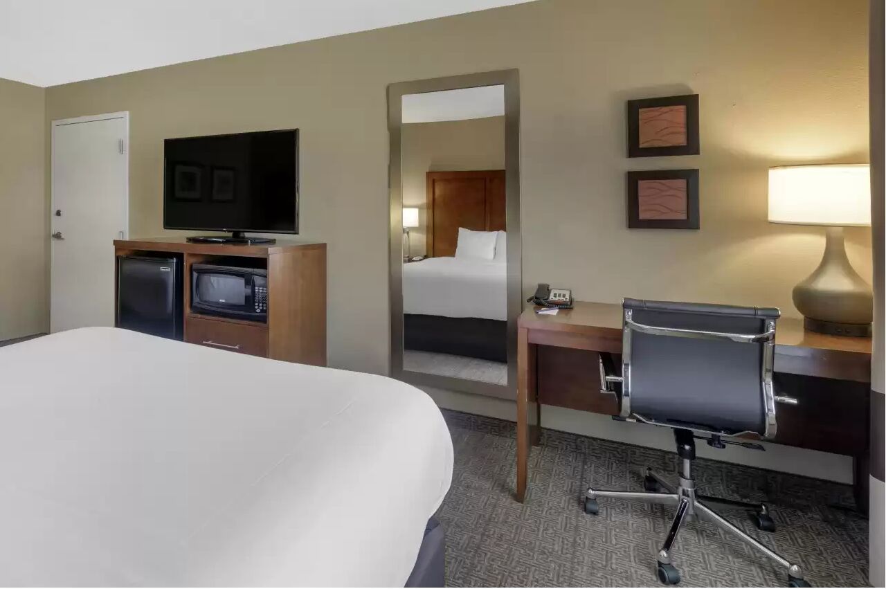 A hotel room with a large bed, a desk with a chair, a television, a microwave, and a small refrigerator.