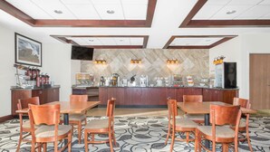 A hotel dining area with a large wooden table, multiple chairs, a coffee station, and a television on the wall. - Ramada by Wyndham Denver International Airport (Denver)
