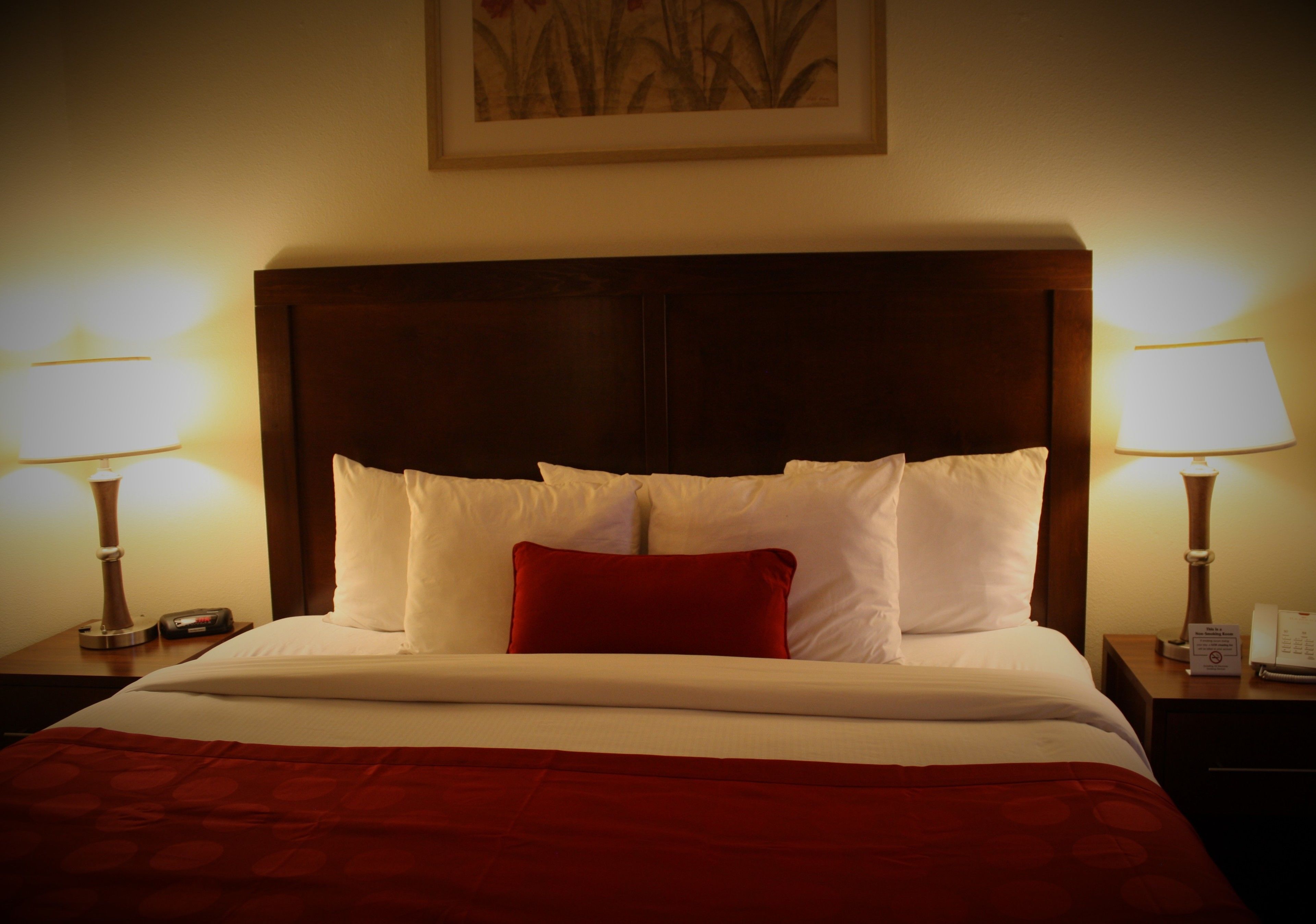 A neatly made bed with white and red bedding, two bedside lamps, and a framed artwork above the bed.