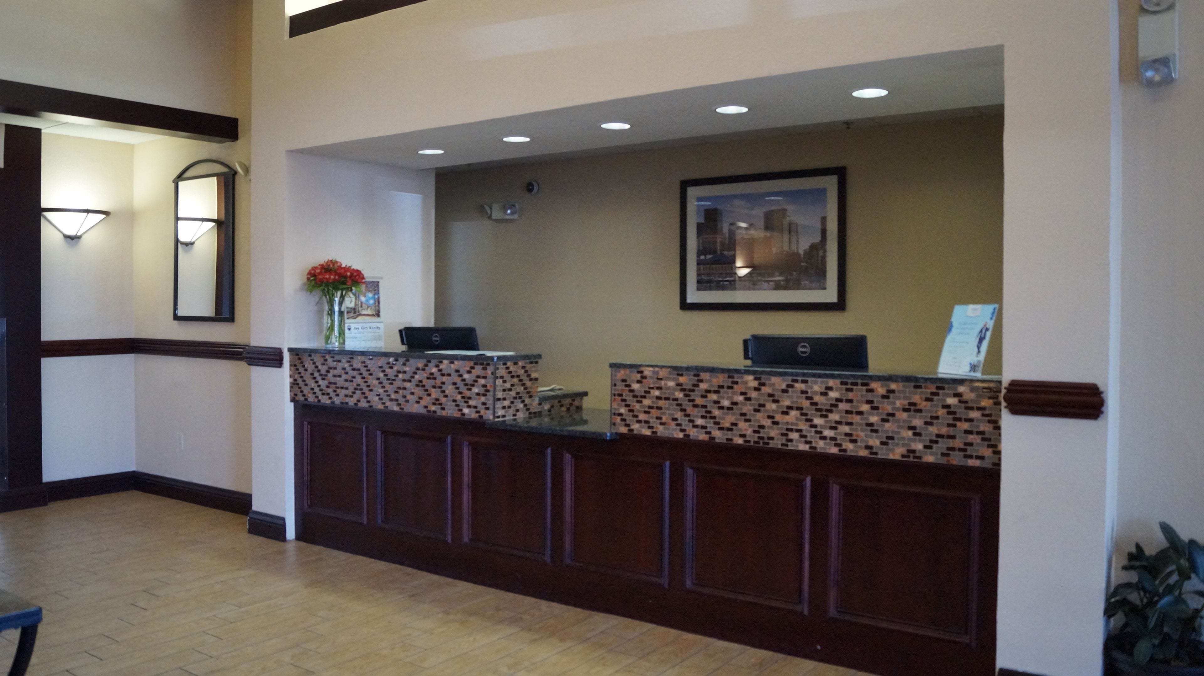 A reception desk with a patterned design, a framed cityscape picture, and a vase with red flowers.