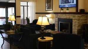 A hotel lobby with a fireplace, comfortable seating, a television, and a window with curtains. - Ramada by Wyndham Denver International Airport (Denver)