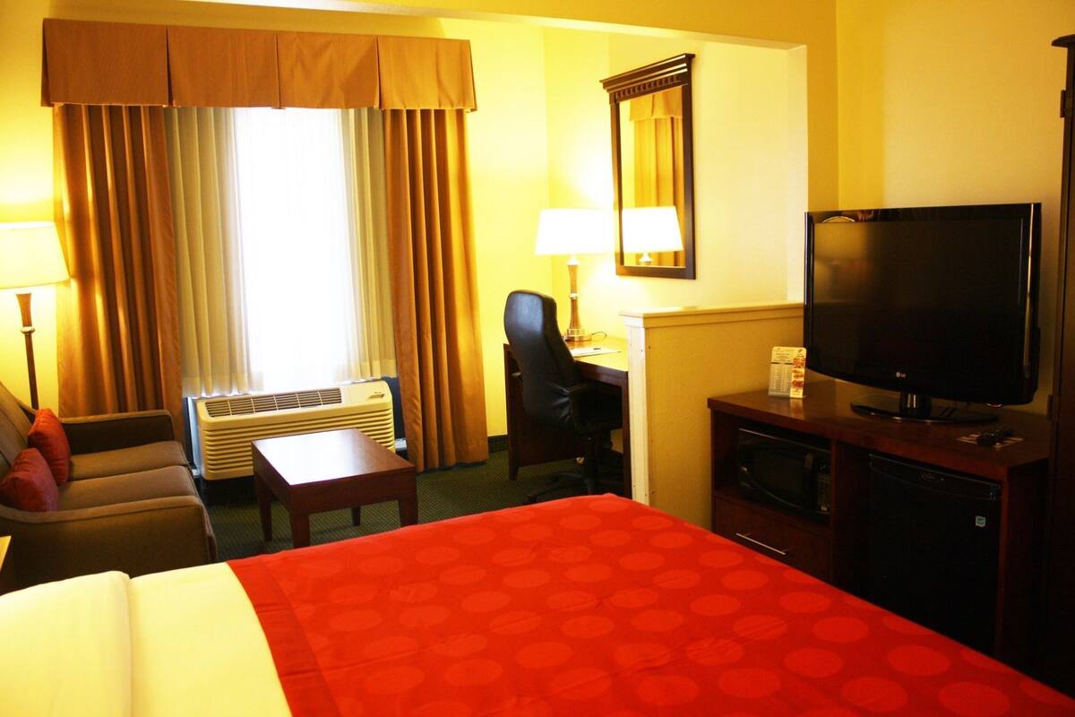 Een hotelkamer met een bed, bureau, stoel, televisie en een raam met gordijnen.