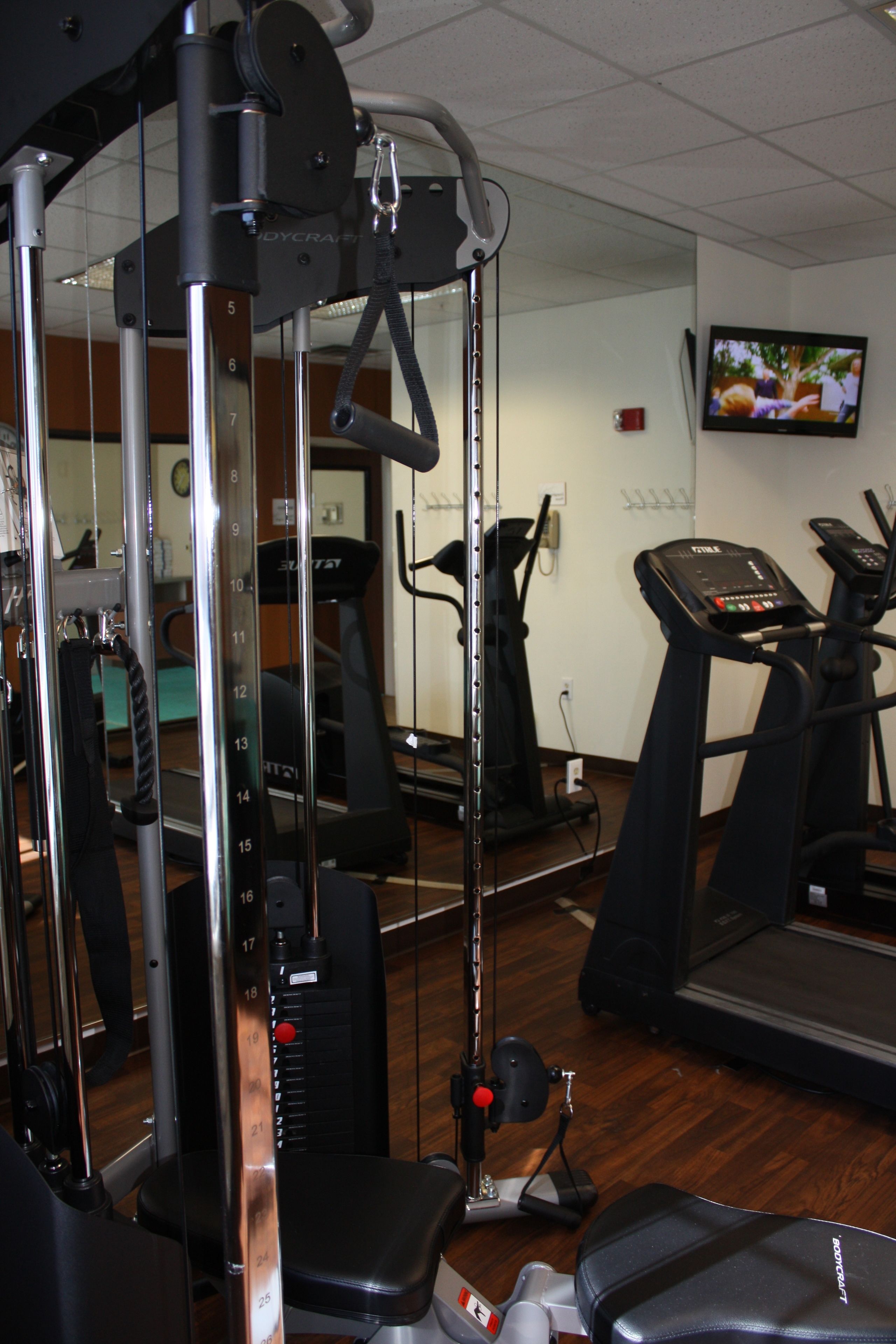 A gym with exercise equipment, a treadmill, and a television mounted on the wall.