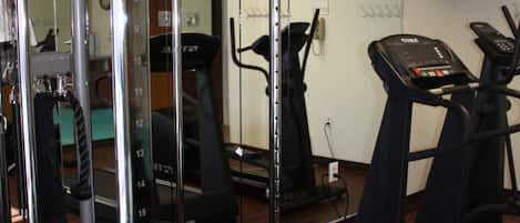Un gimnasio con equipo de ejercicio, cinta de correr y televisor montado en la pared.