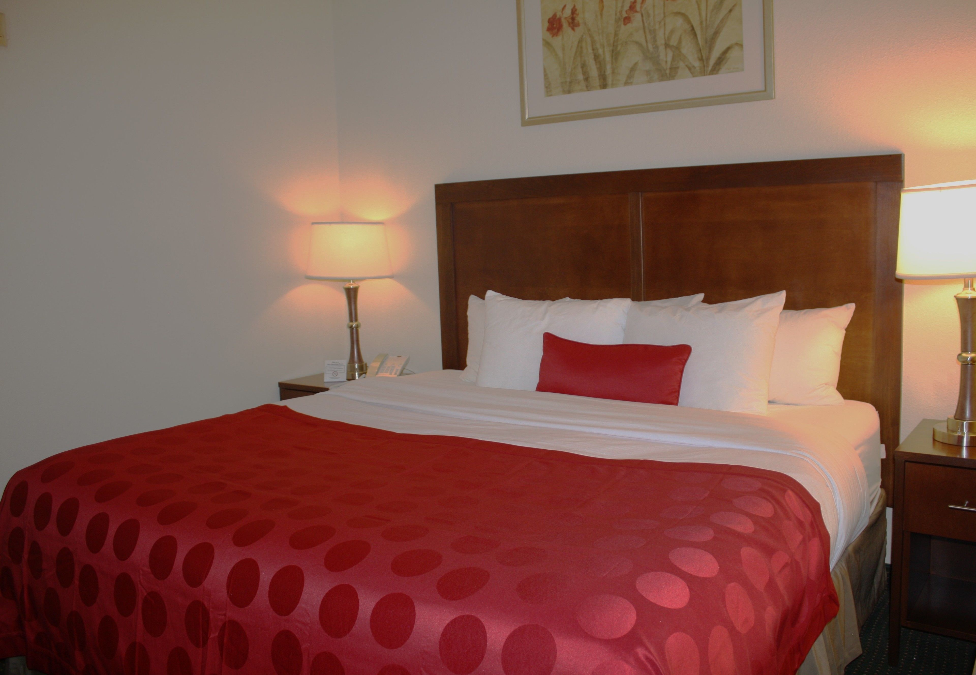 Una habitación de hotel con una cama grande, dos mesitas de noche y una mesilla auxiliar con lámpara.