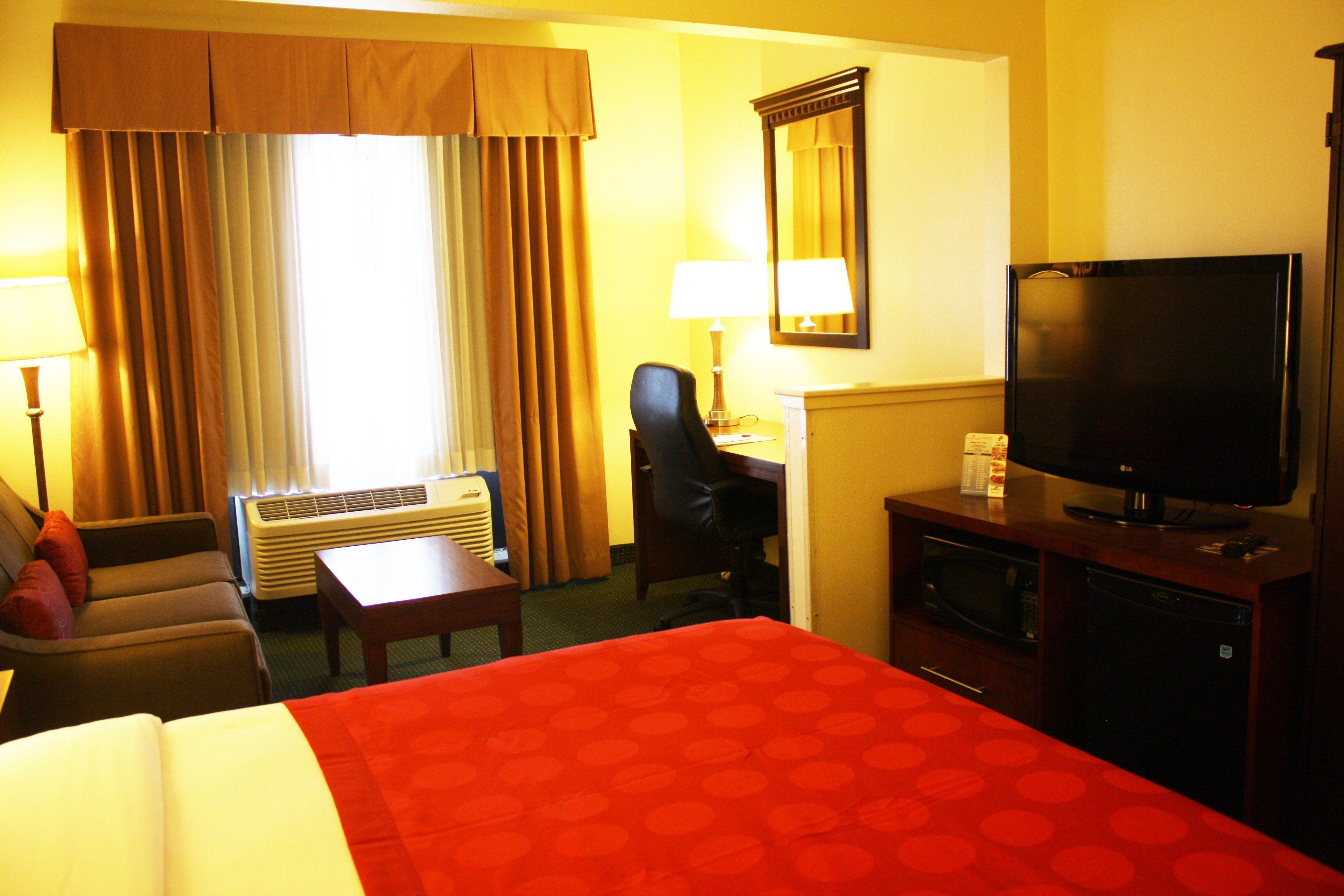 Una habitación de hotel con cama, escritorio, silla, televisor y aire acondicionado.
