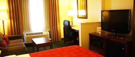 Una habitación de hotel con cama, escritorio, silla, televisor y aire acondicionado.