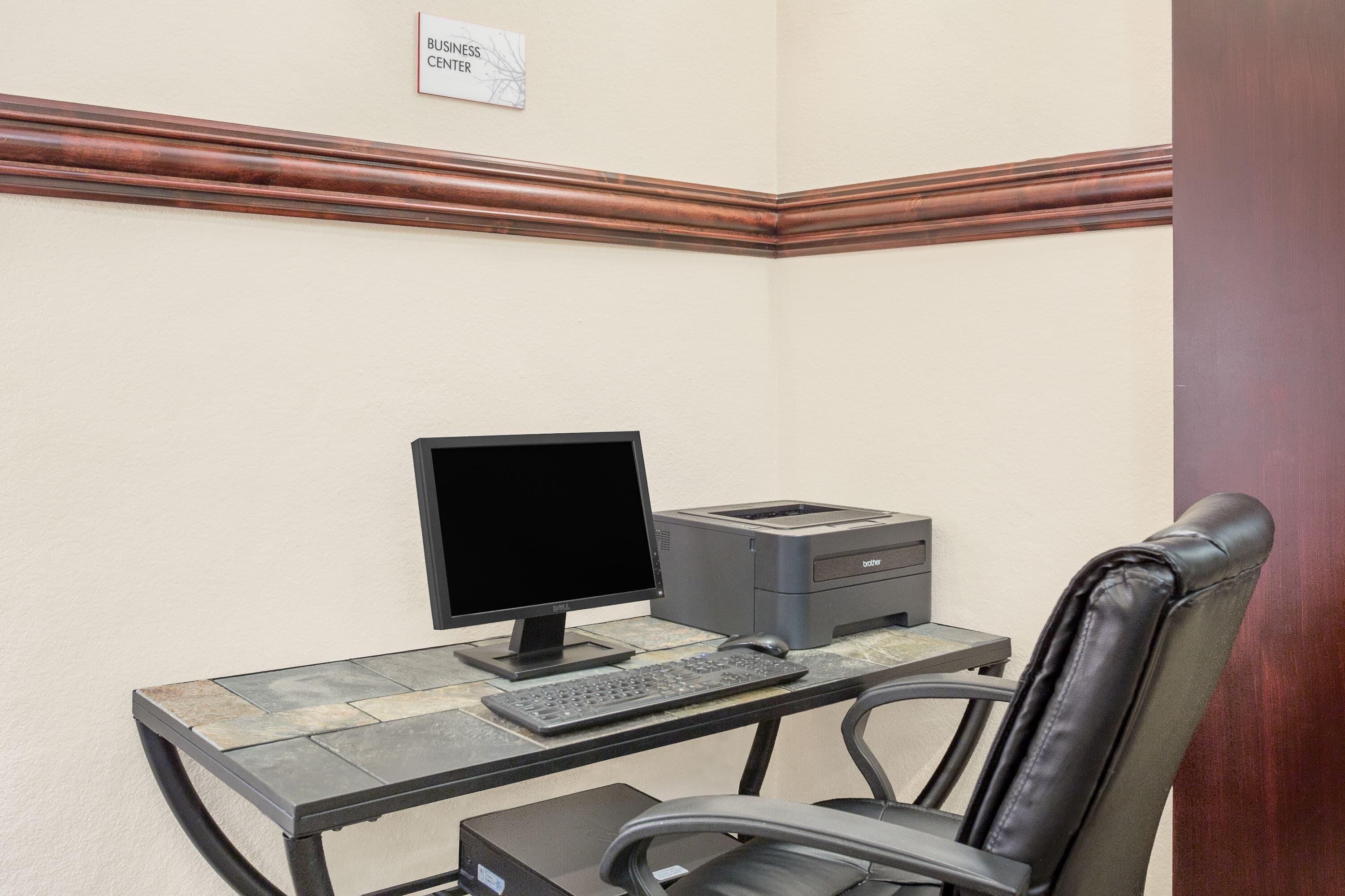 Oficina en esquina con escritorio, computadora, impresora y sillón de cuero.