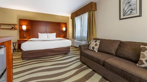 A hotel room with a bed, a sofa, a desk, a wall-mounted TV, and a framed picture. - Quality Inn & Suites Stoughton - Madison South (Stoughton)