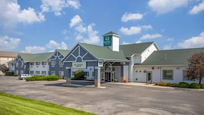 A hotel with a green roof, a sign indicating 'Quality Inn & Suites,' and a parking lot with a few cars. - Quality Inn & Suites Stoughton - Madison South (Stoughton)