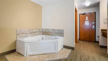 A bathroom with a white bathtub, beige walls, and a patterned floor.