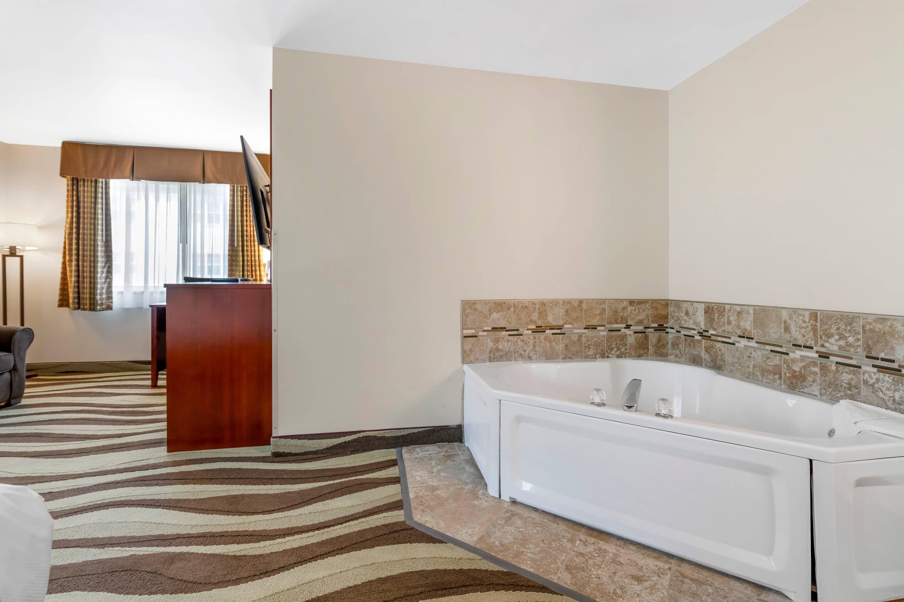 A modern bathroom with a large bathtub, a wooden desk, and a television.