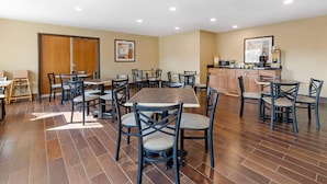 A dining area with multiple tables and chairs, a kitchen area with cabinets and appliances, and a wooden door. - Quality Inn & Suites Stoughton - Madison South (Stoughton)