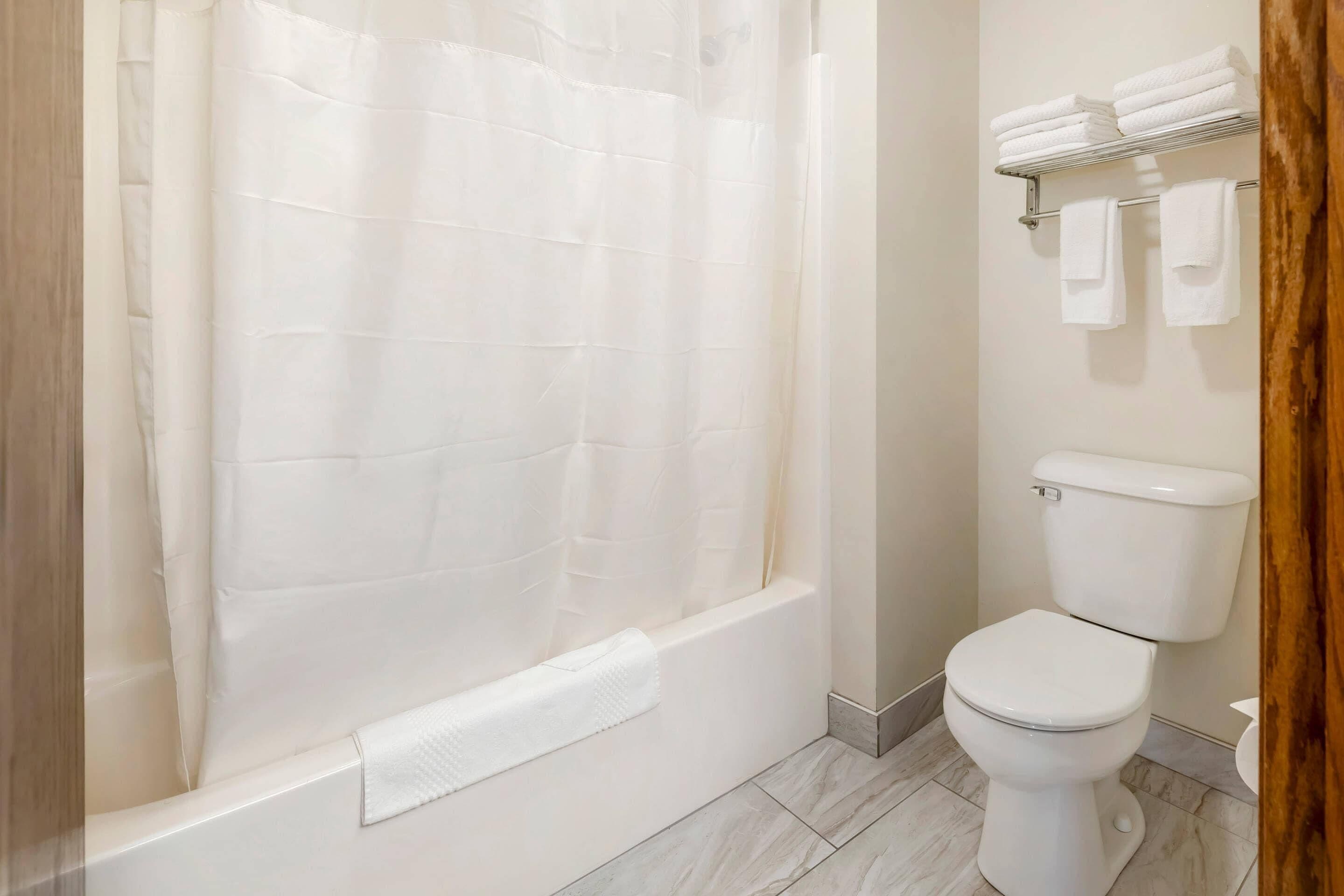 A bathroom with a bathtub, toilet, and a shelf with towels.