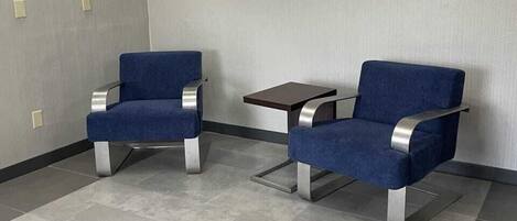 Une pièce moderne avec deux fauteuils bleus et une petite table, des murs de couleur gris clair et un sol carrelé.