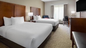 A hotel room with two beds, a desk, a chair, a TV, and a window with curtains.