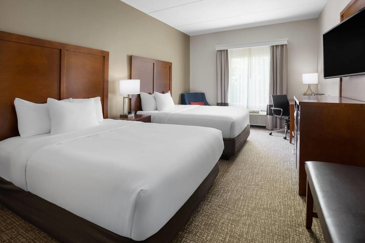 A hotel room with two beds, a desk, a chair, a TV, and a window with curtains.