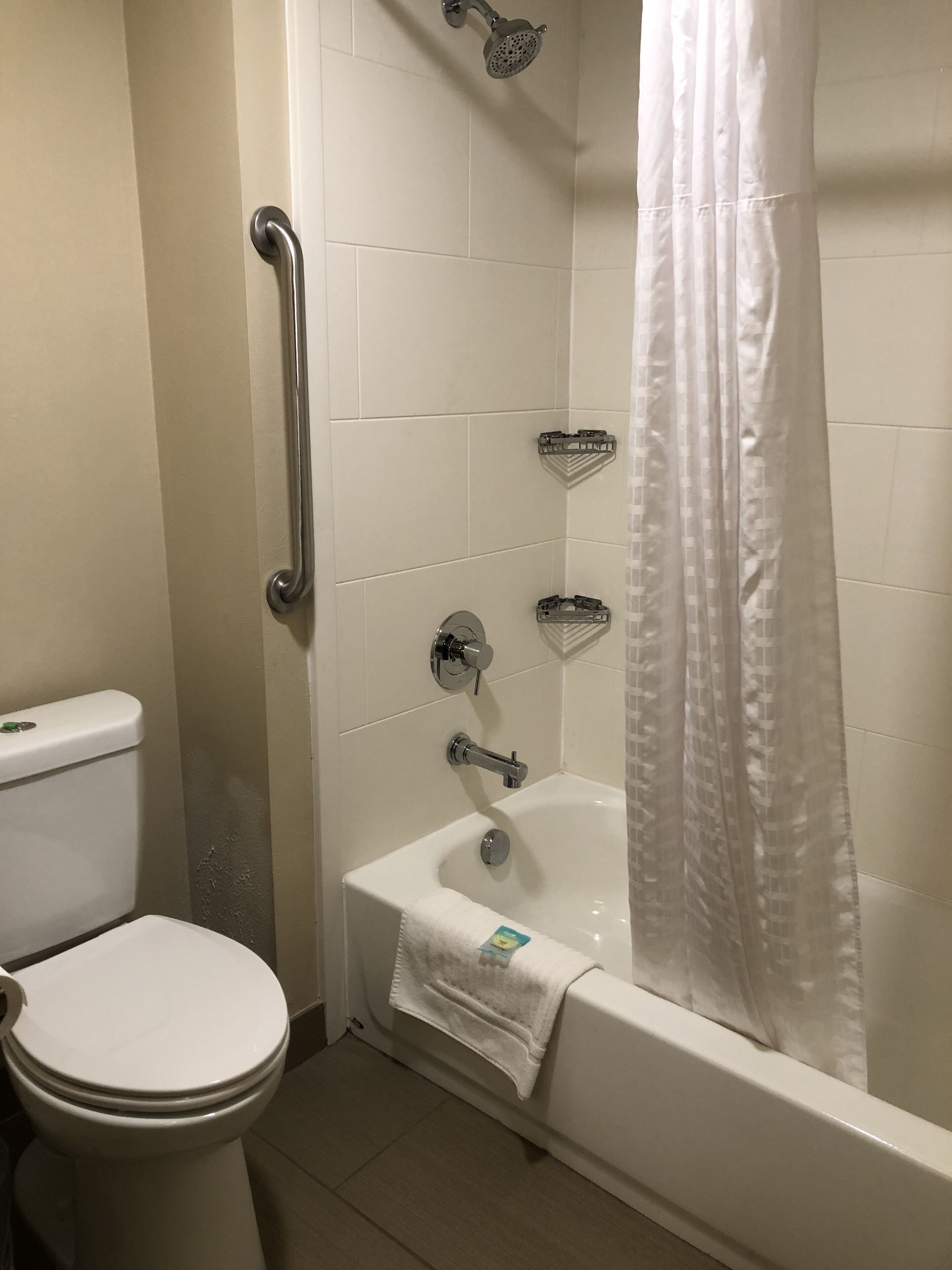 Une salle de bain équipée de toilettes, d’une douche avec rideau et d’une barre d’appui.