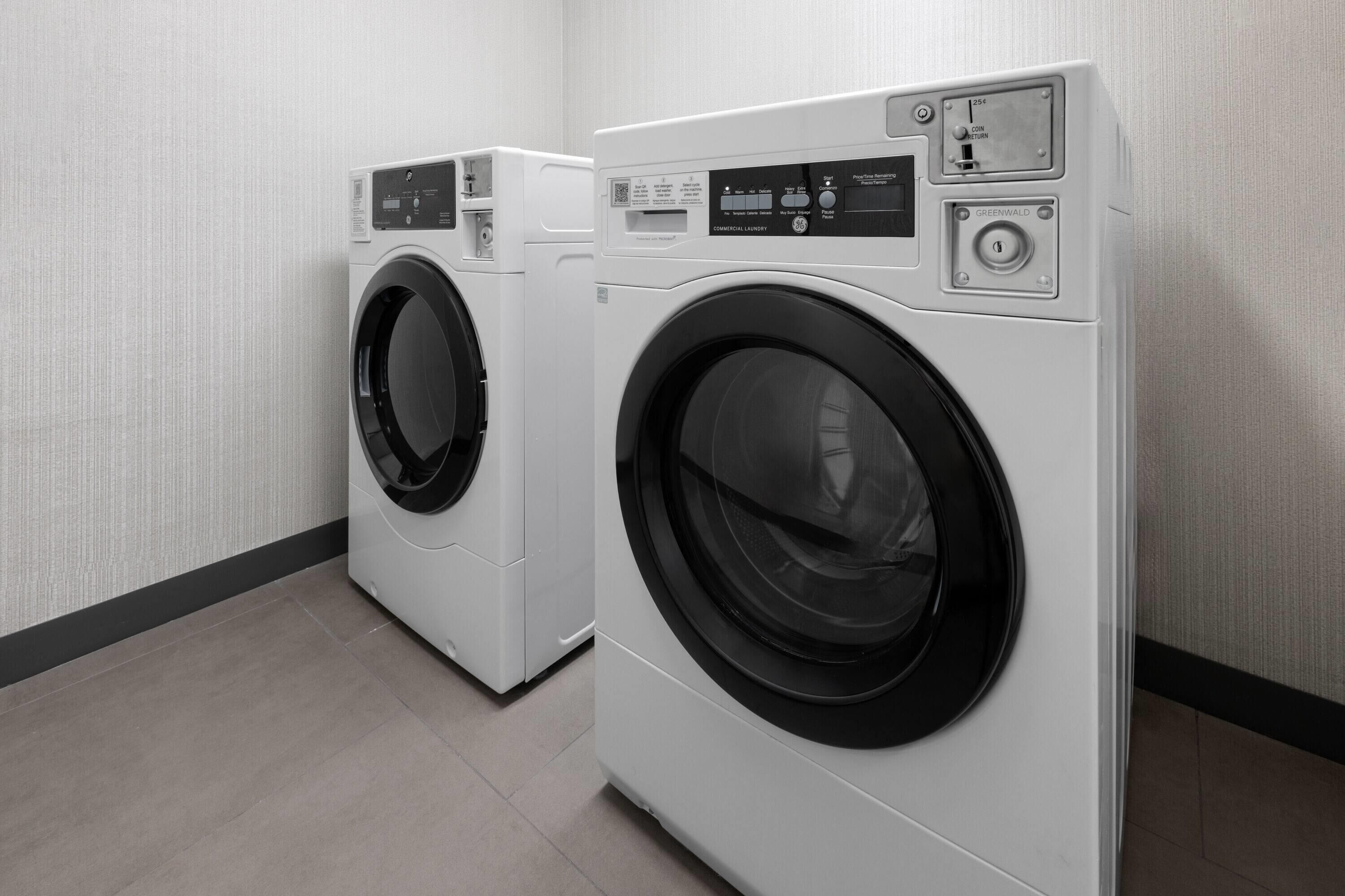 Twee voorladers wasmachines in een wasserette met een betegelde vloer en een structuurwand.