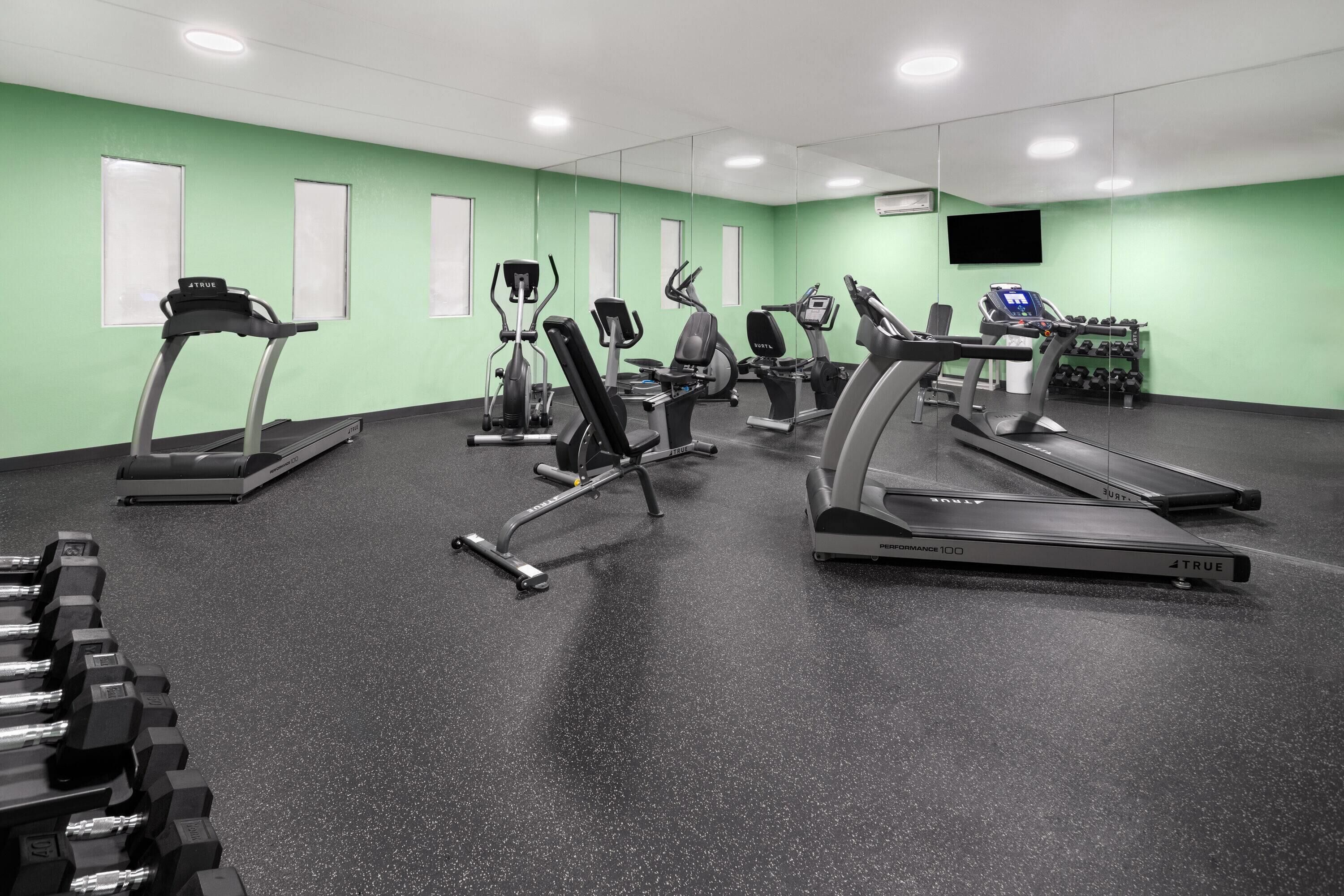 Une salle de sport équipée de tapis de course, de vélos elliptiques et d’haltères.