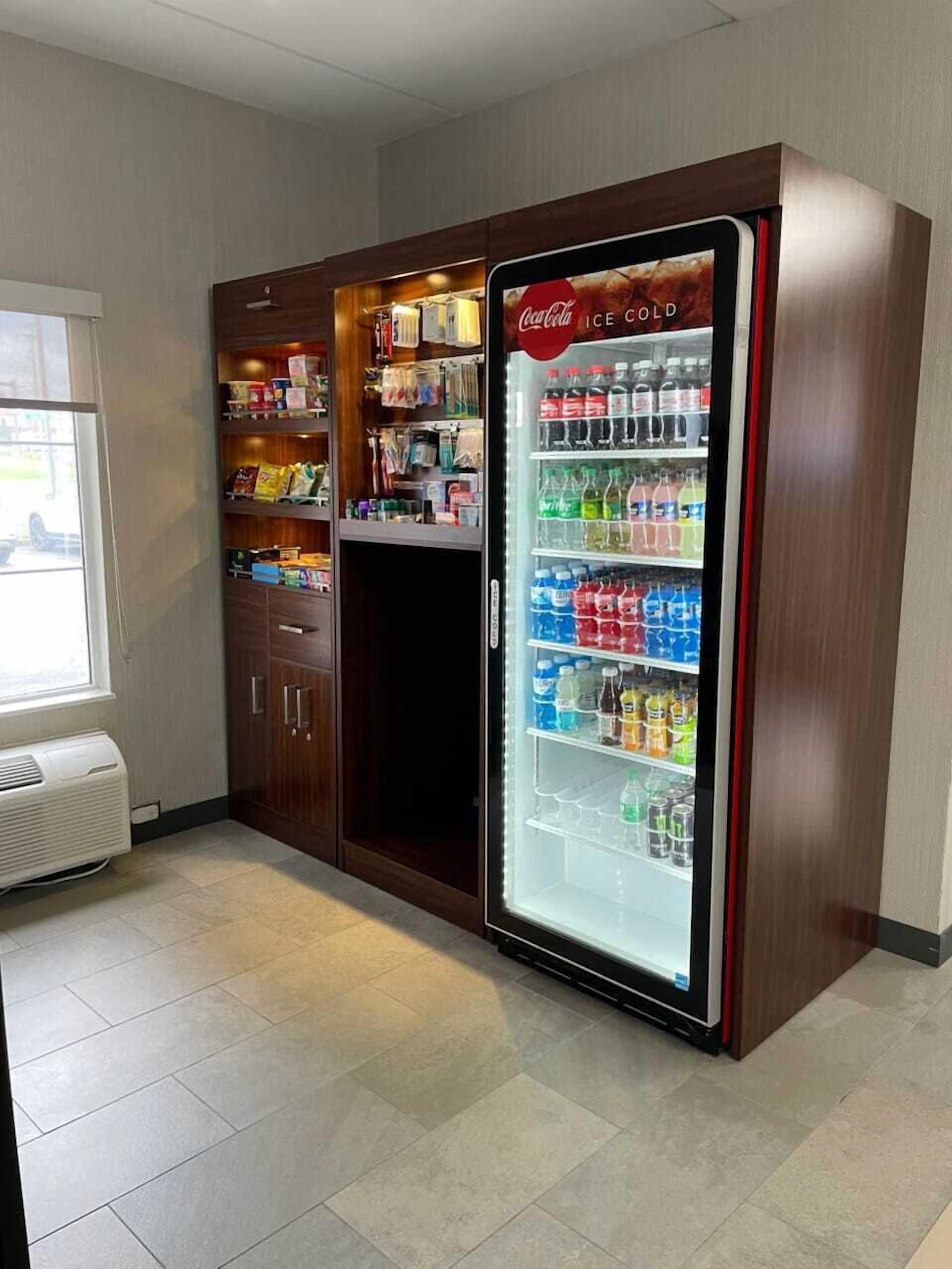 A Coca-Cola refrigerator stocked with various beverages, a vending machine with snacks, and a window with a view.