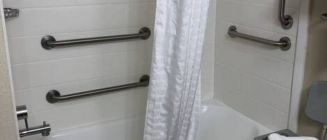 Eine weiße Badewanne mit Haltegriffen, ein weißer Duschvorhang und eine rollstuhlgerechte Sitzbank.