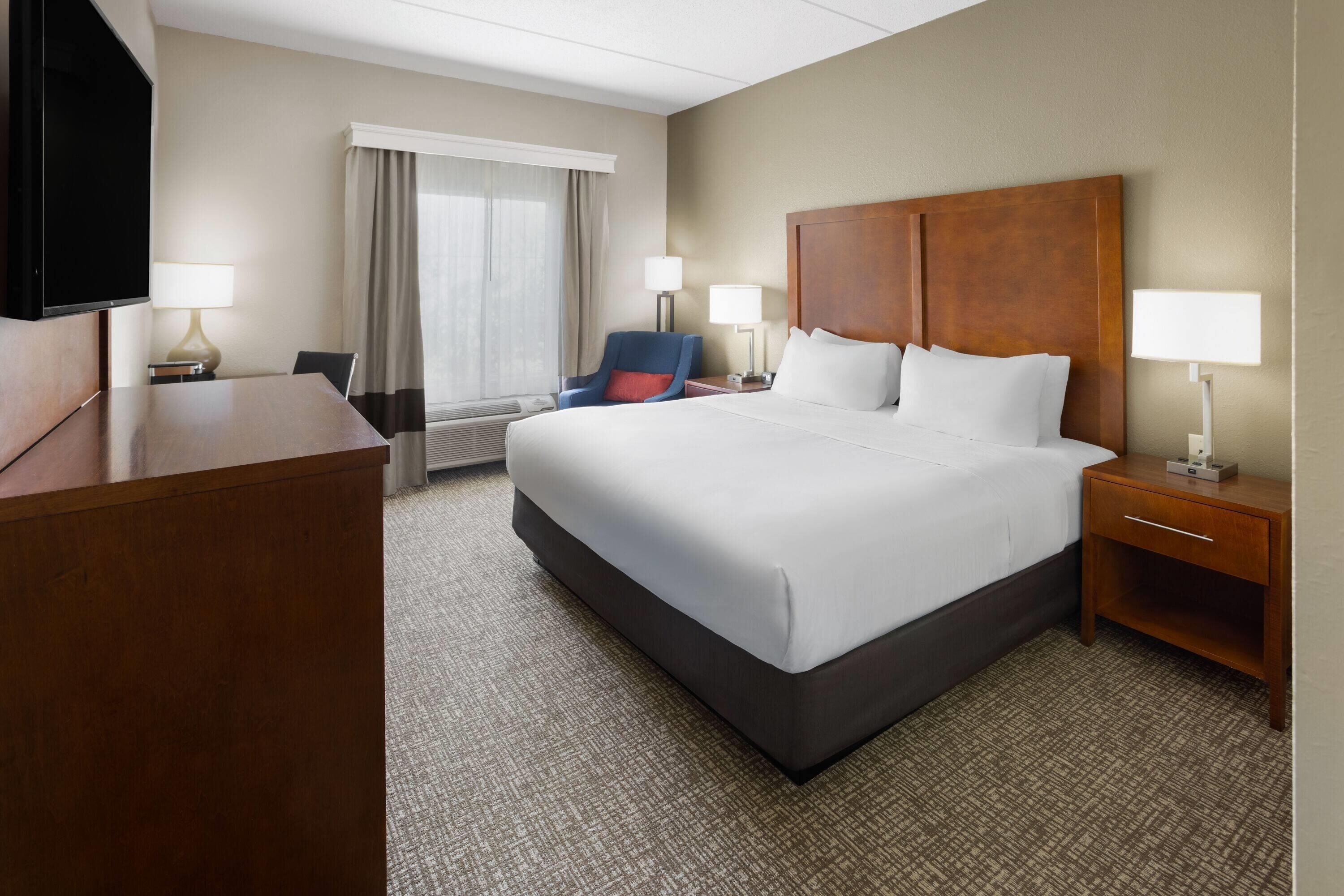 A hotel room with a large bed, a desk, a chair, a TV, and a window with curtains.