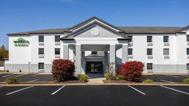 A Wingate hotel with a symmetrical facade, a central entrance with a pediment, and a parking lot in front.