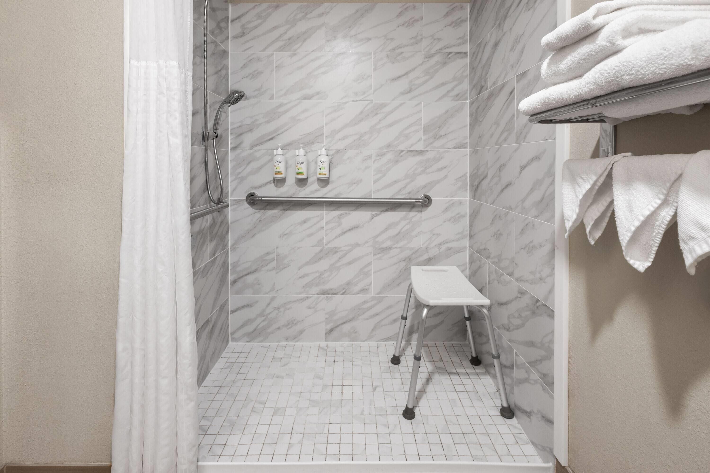 A shower area with a grab bar, a step stool, and toiletries on the wall.