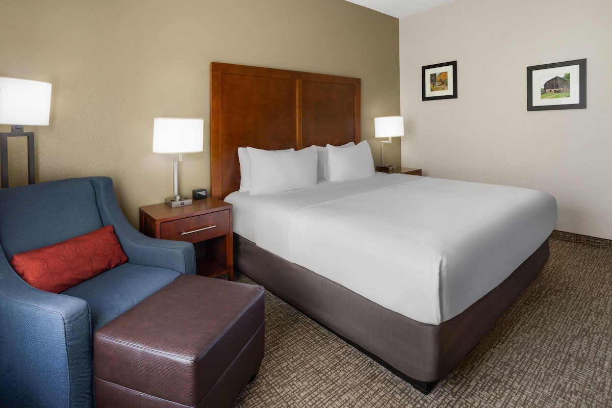 A hotel room with a large bed, a blue armchair, a wooden nightstand, and two wall-mounted lamps.