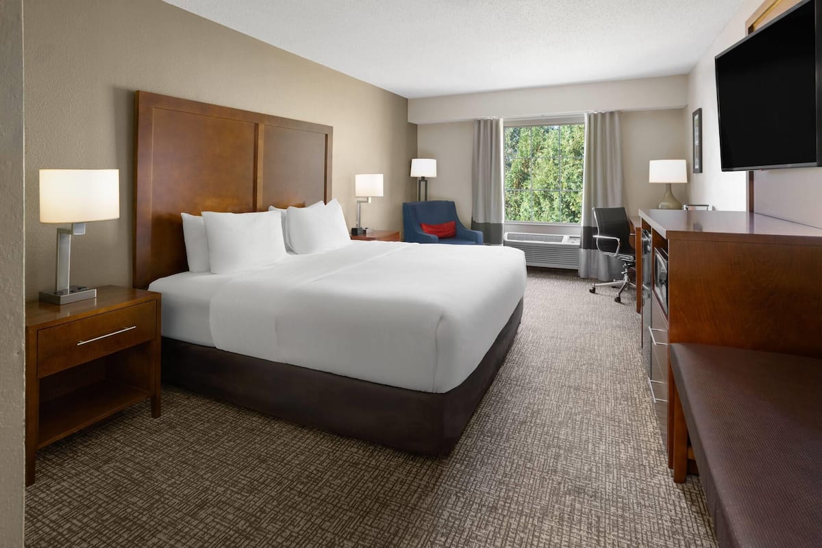 A hotel room with a large bed, bedside tables, a desk, a chair, and a TV.