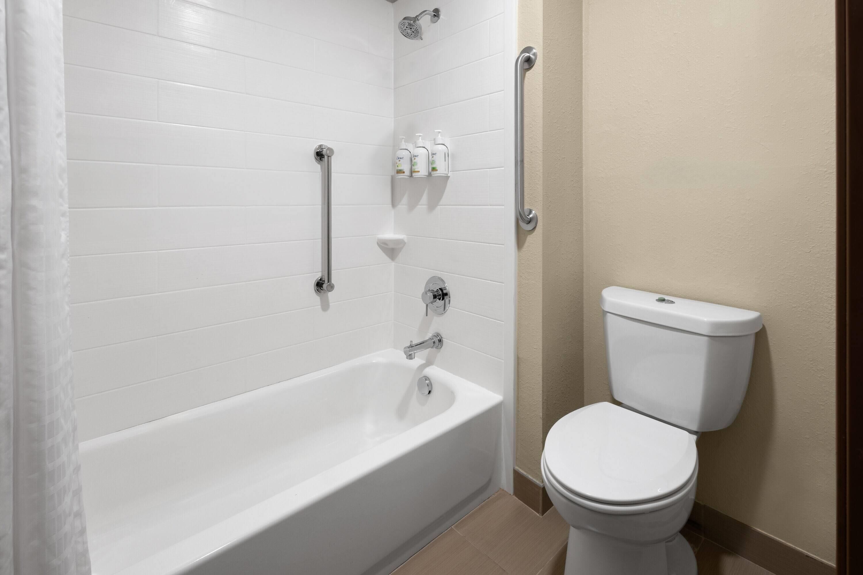 Un baño con una bañera blanca, inodoro y cabezal de ducha.