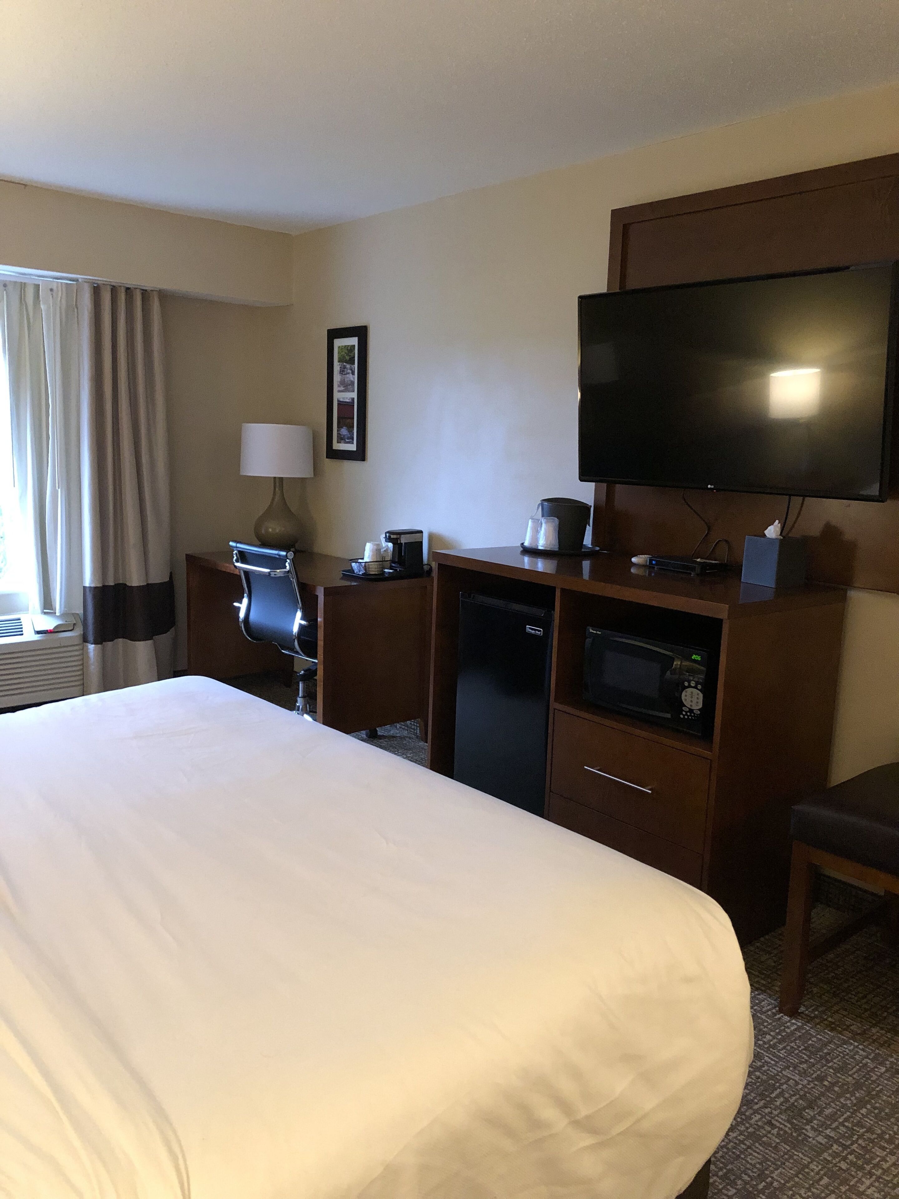 Una habitación de hotel con una cama grande, un escritorio con lámpara, televisor, microondas y refrigerador.
