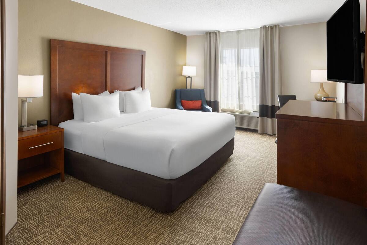 A hotel room with a large bed, a desk, a chair, and a television.