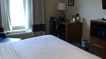 Une chambre d’hôtel avec un grand lit, un bureau avec une lampe, une chaise, une télévision et une fenêtre avec des rideaux.