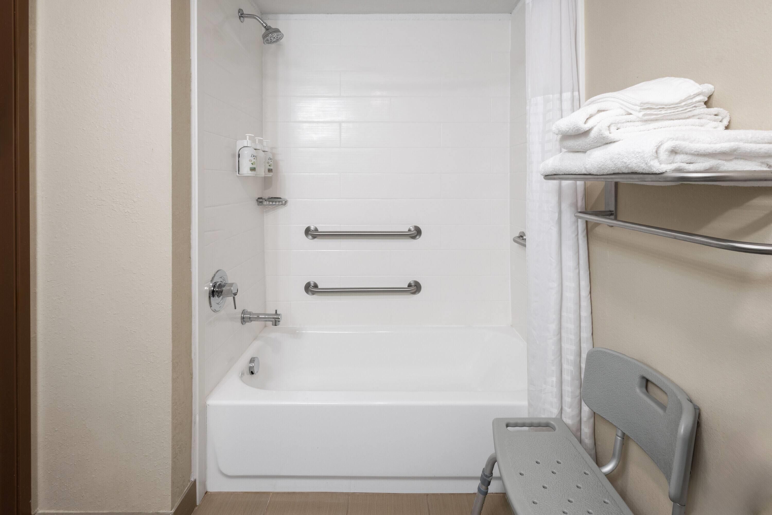 A bathroom with a white bathtub, grab bars, a showerhead, a towel rack, and a shower chair.