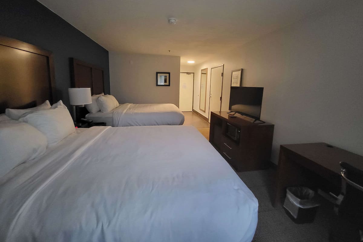 A hotel room with two beds, a desk, a TV, and a trash bin.