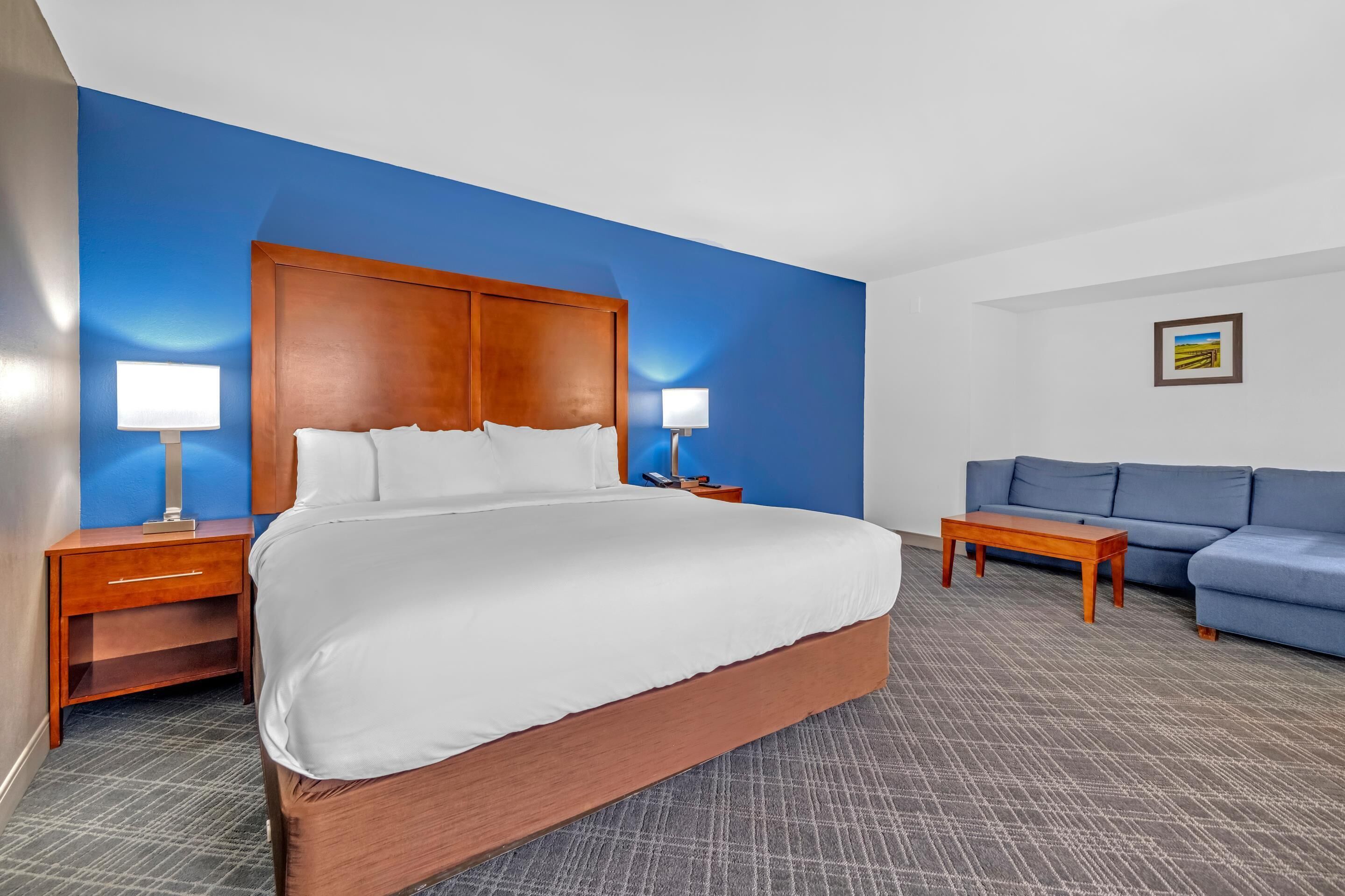 A hotel room with a large bed, two bedside tables with lamps, a blue sofa, and a small wooden table.