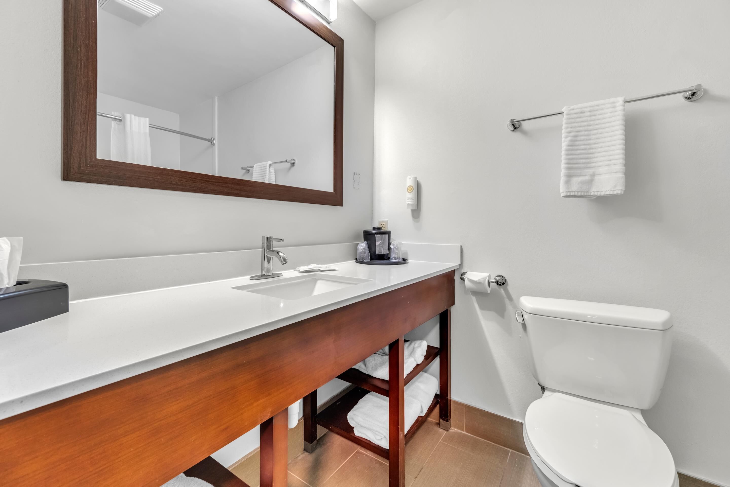 Un baño moderno con tocador de madera, un espejo grande, un inodoro blanco y un perchero para toallas.