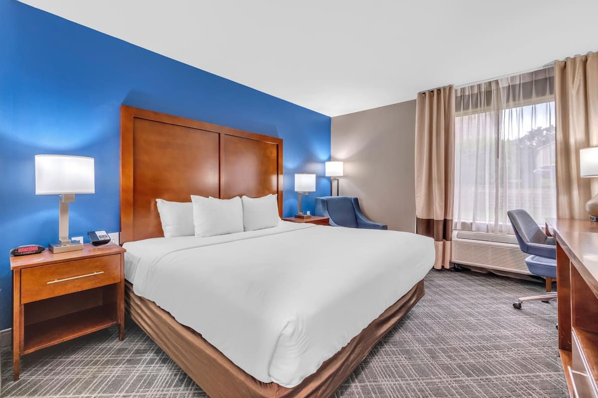 A hotel room with a large bed, bedside tables with lamps, a desk, and a chair.