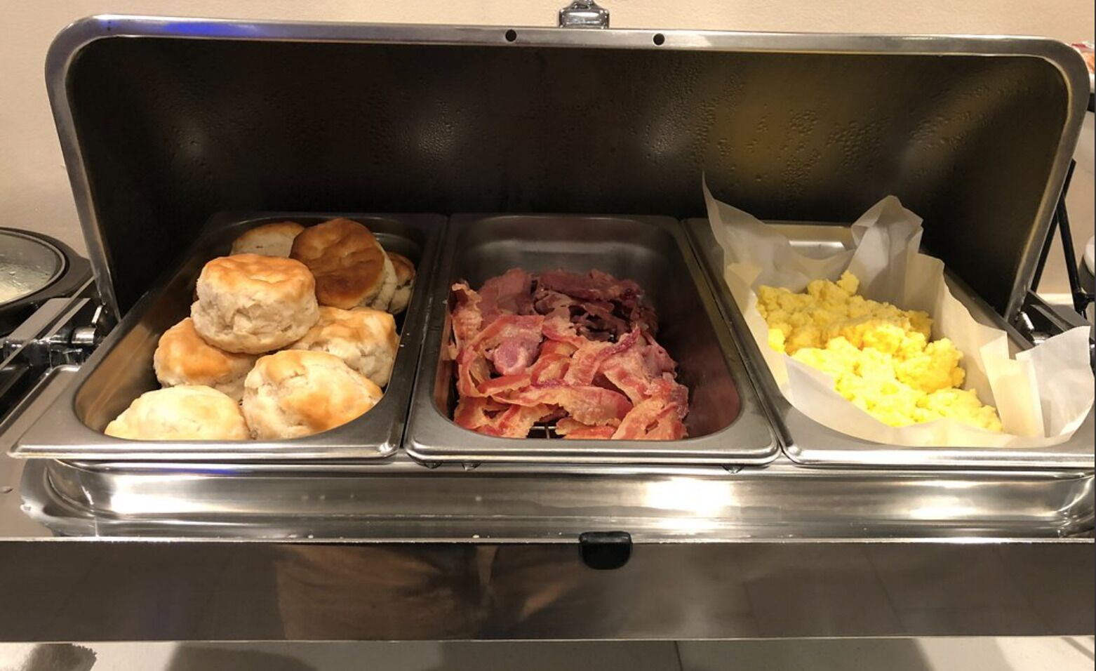 A buffet with three food stations: biscuits, bacon, and scrambled eggs.